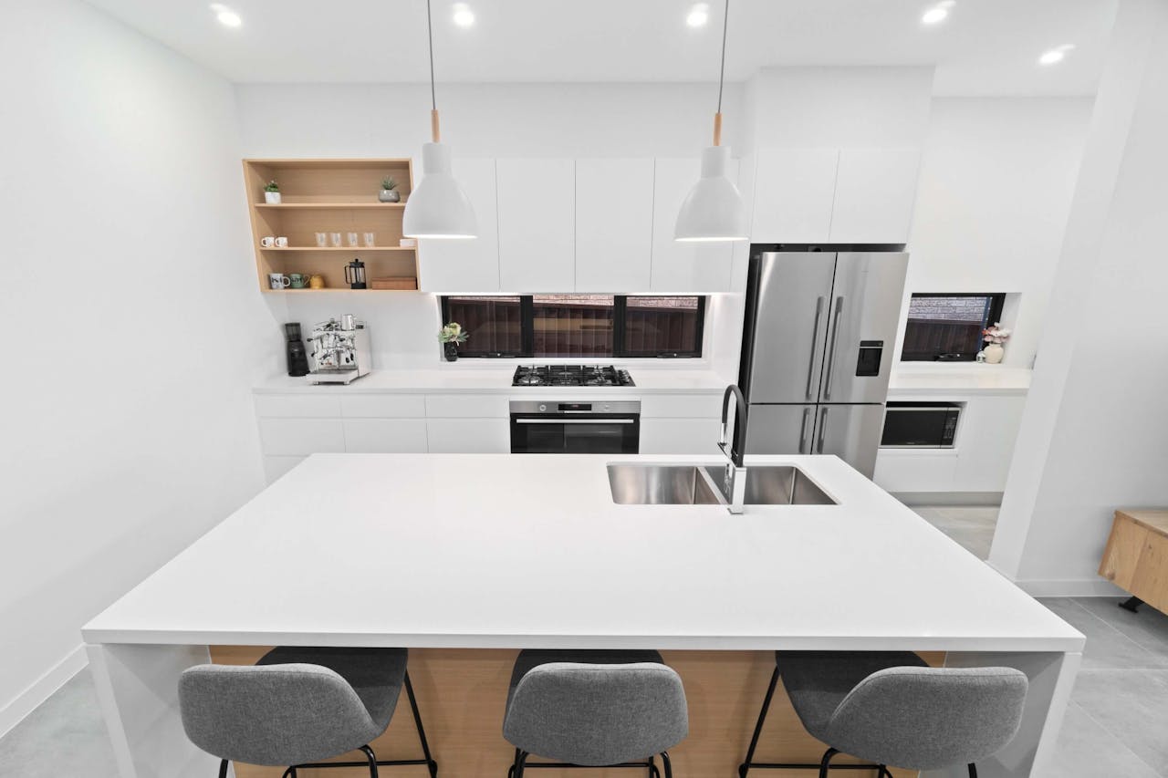 gallery-04 Sleek and minimalist white kitchen with island and hanging lights, perfect for modern homes.