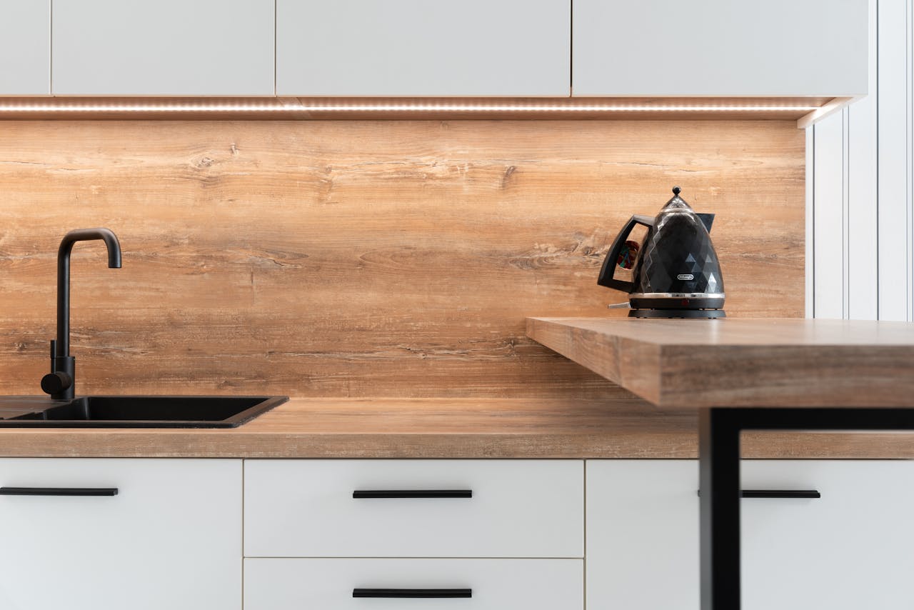 our-story A sleek modern kitchen with wooden backsplash and black kettle, highlighting minimalist design.